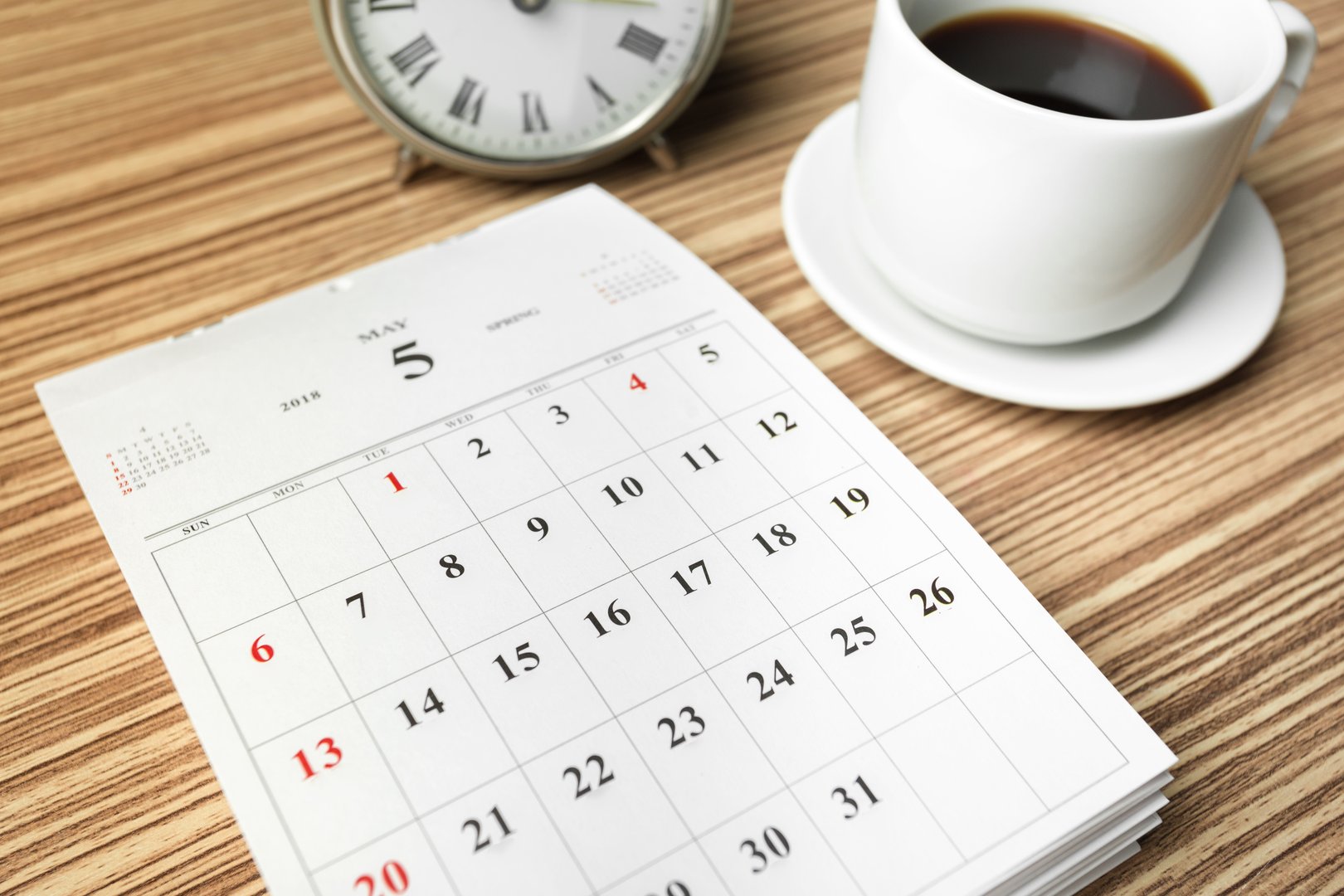 A cup of black coffee sits beside a clock and a calendar marked for an important date.