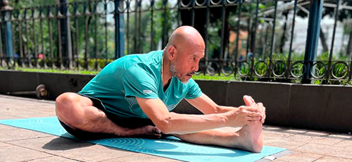 Man practicing seated forward bend yoga pose on a mat outdoors.