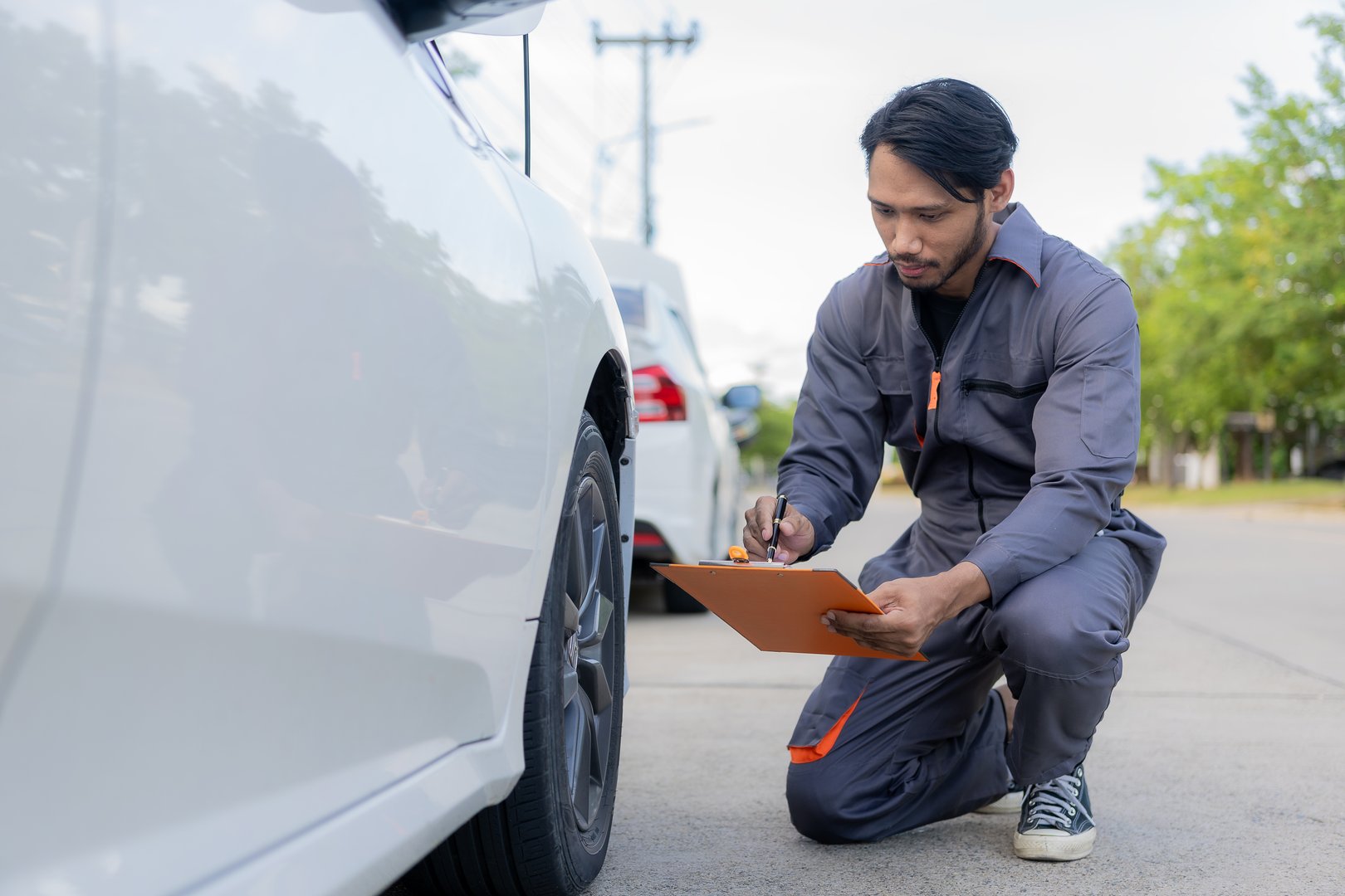 maintenance concept Asian auto mechanic or smith writing on clipboard at warehouse workshop Technician making checklist for car repair Roadside breakdown and insurance concept