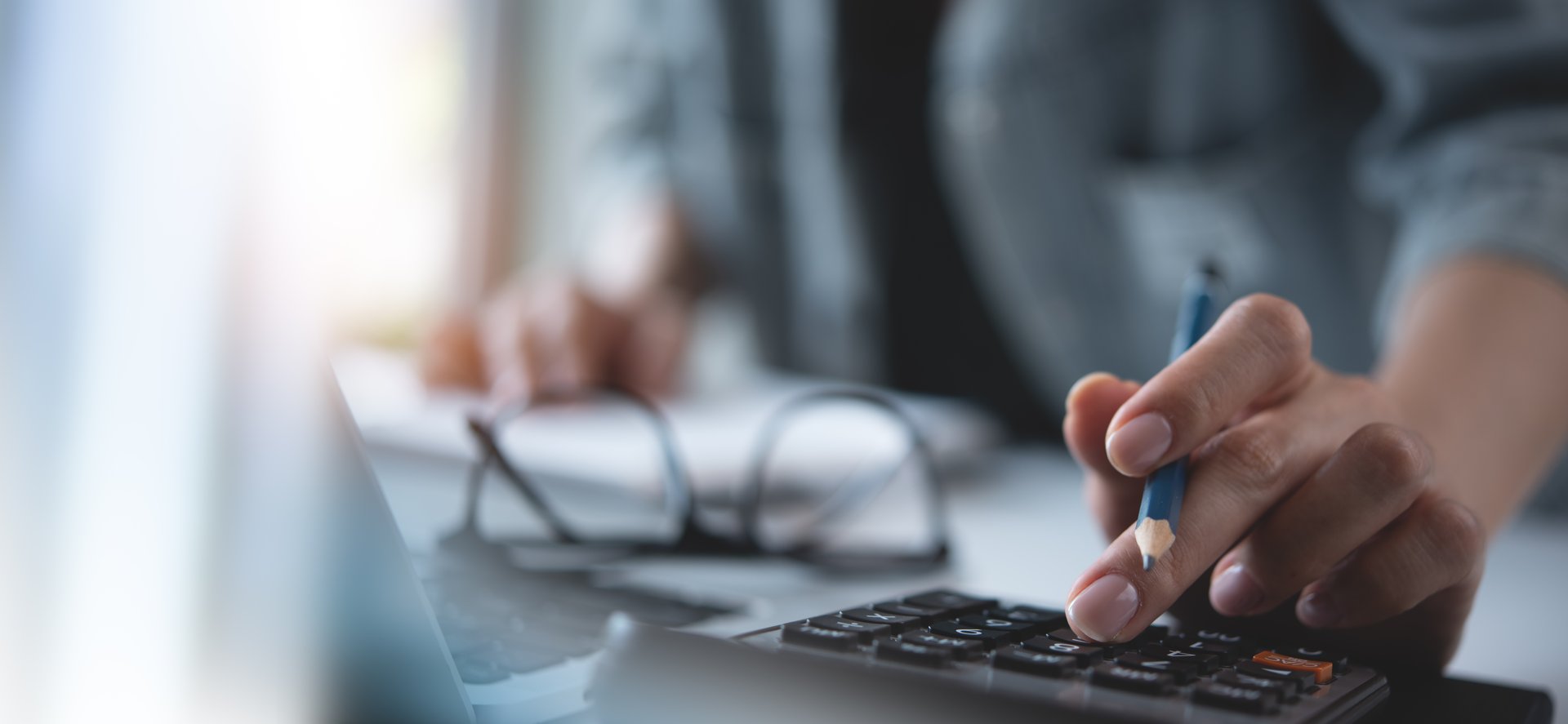 Doing finance, budgeting and tax calculation. Close up woman hand using calculator to calculate home finance and writing note, accounting with laptop computer on table, budget management