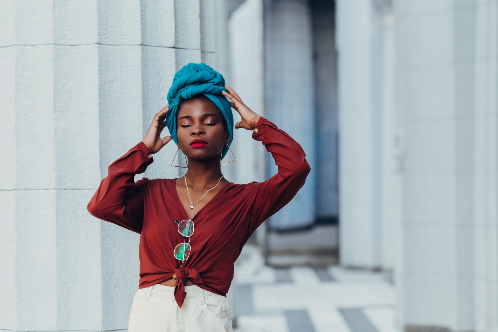 Outdoor  portrait of a fashionable muslim african woman"nwears white high-waisted jeans, an orange blouse and blue headscarf "nPosing on the street