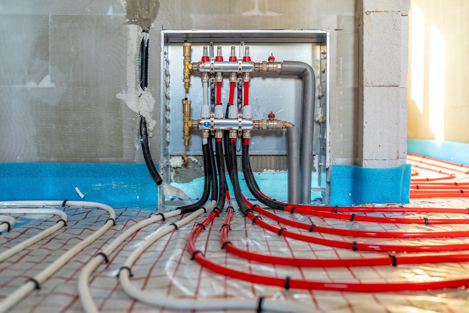 Red and white plastic pipes of an underfloor heating system being installed on insulation, connecting seamlessly to the distribution system for optimal energy efficiency and warmth