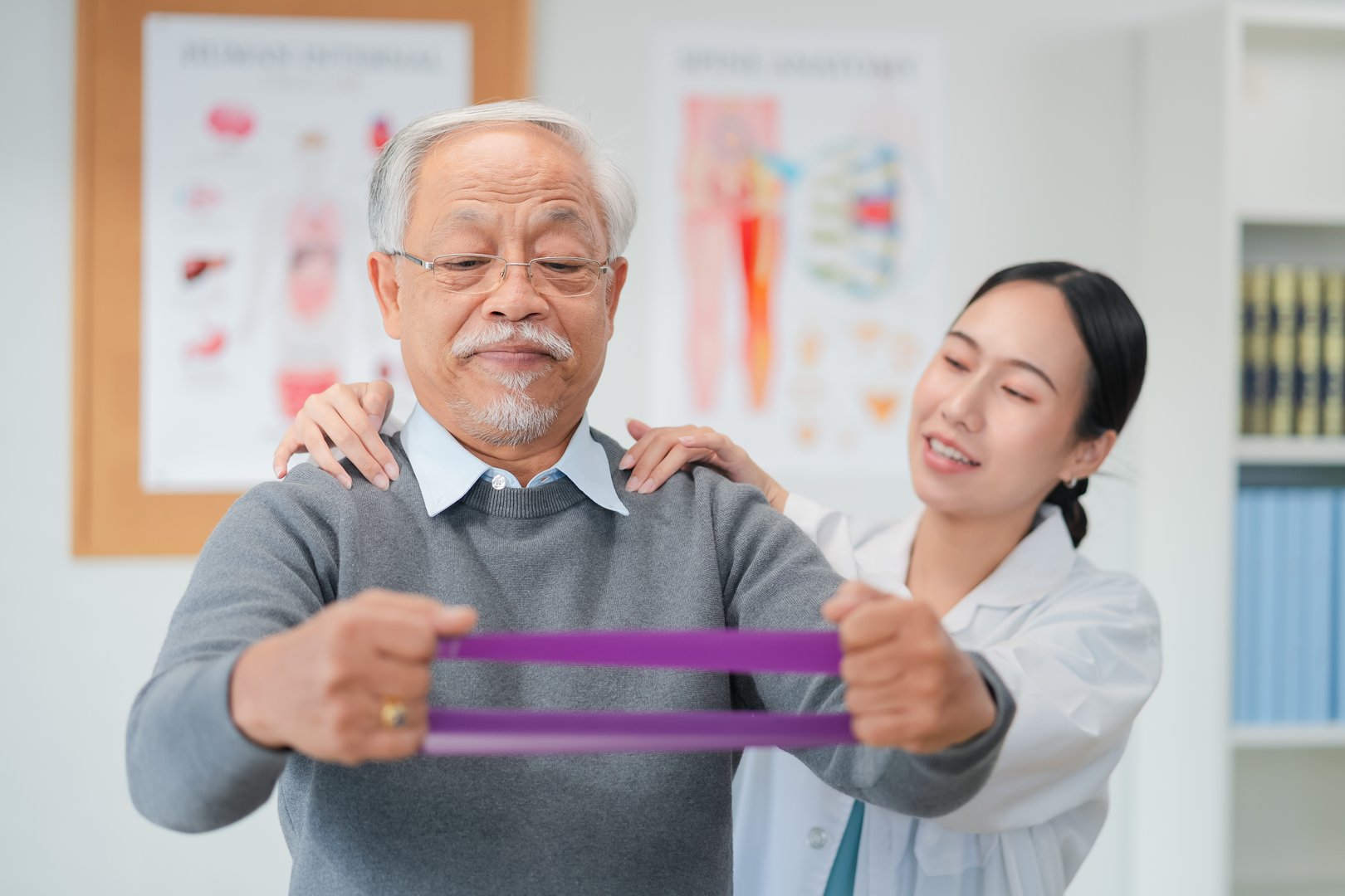A caring physical therapist guides a senior Asian woman through resistance band exercises during a rehabilitation session, helping her improve strength, mobility, and confidence. supportive therapy