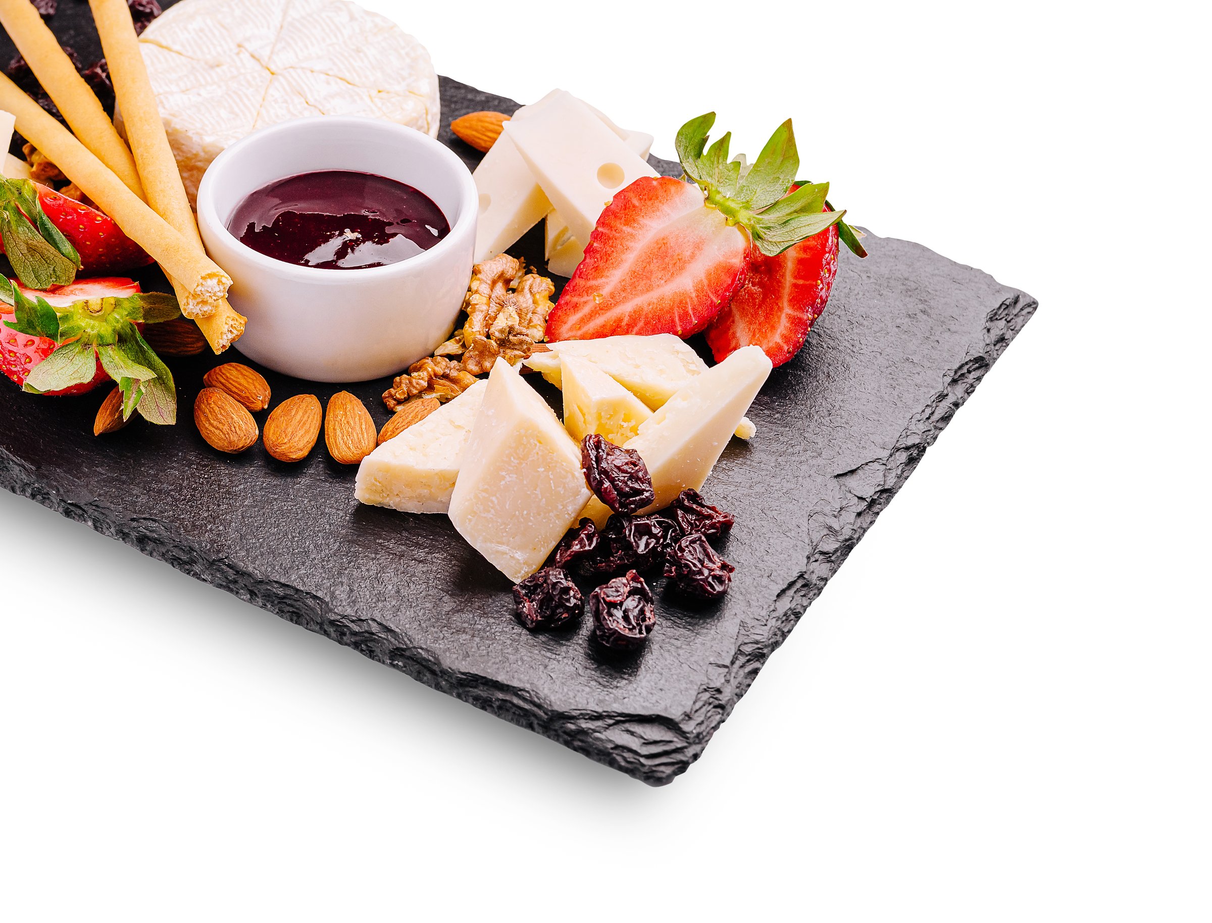 A beautifully arranged cheese platter features assorted cheeses, fresh strawberries, nuts, and a small bowl of jam. This exquisite spread is perfect for gatherings and celebrations.