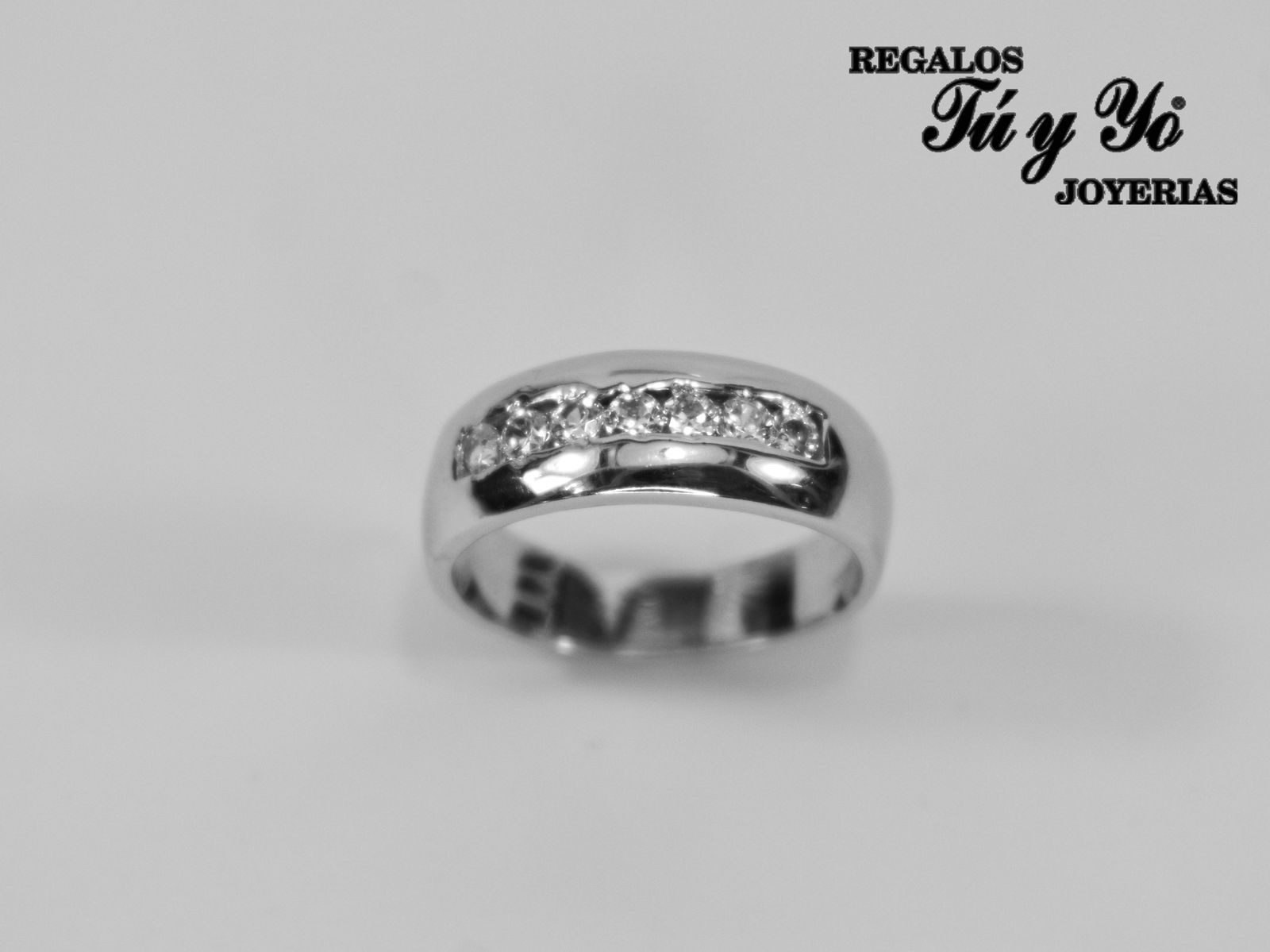 Silver ring with a row of embedded diamonds, shown against a plain background. Branding text in the corner says "Regalos Tú y Yo".