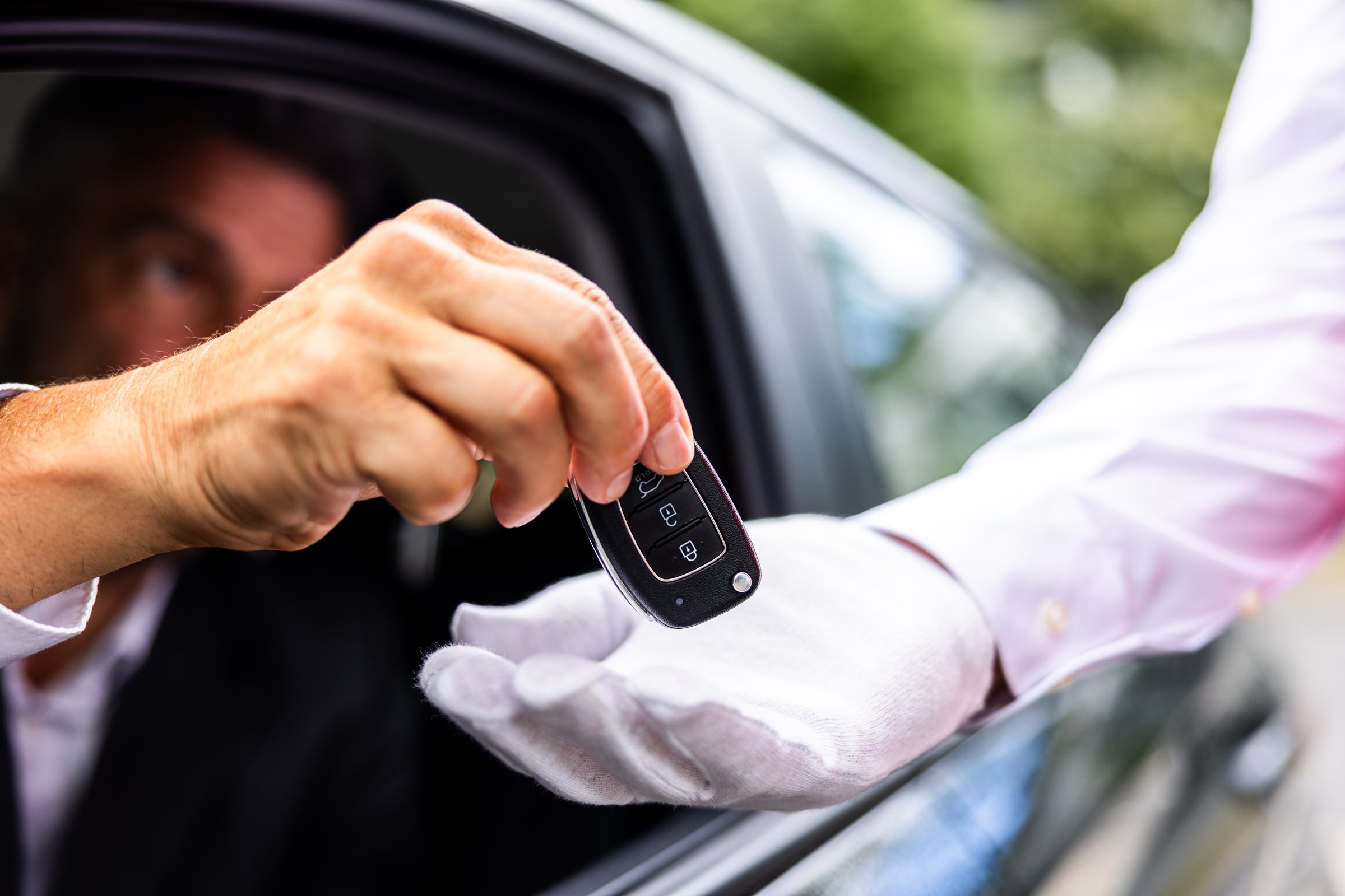 Luxury chauffeur service at a hotel: a businessperson's hand giving car key to valet in the city, ensuring excellence.