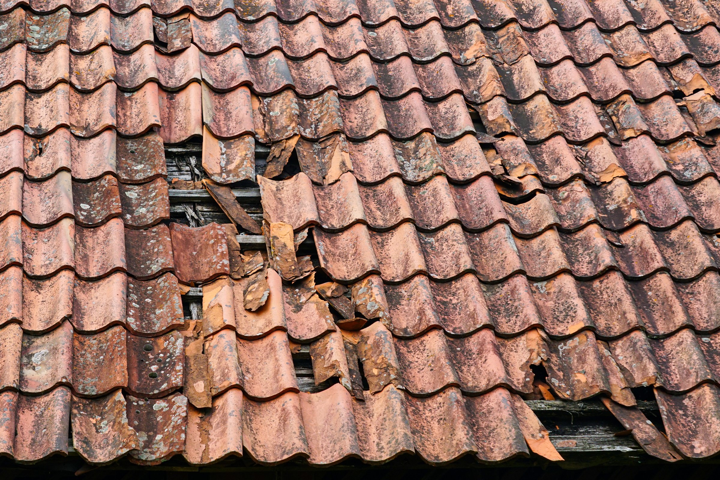 Dangerously damage to the clay tile roof of a historic house with some roof tiles missing, broken roof tiles, hole in roof