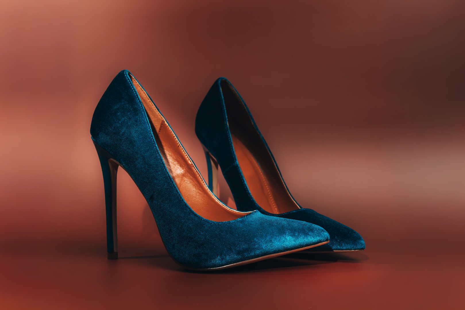 Two blue high heels with glitter on them. The heels are on a red background. The shoes are shiny and sparkly, giving off a glamorous and elegant vibe