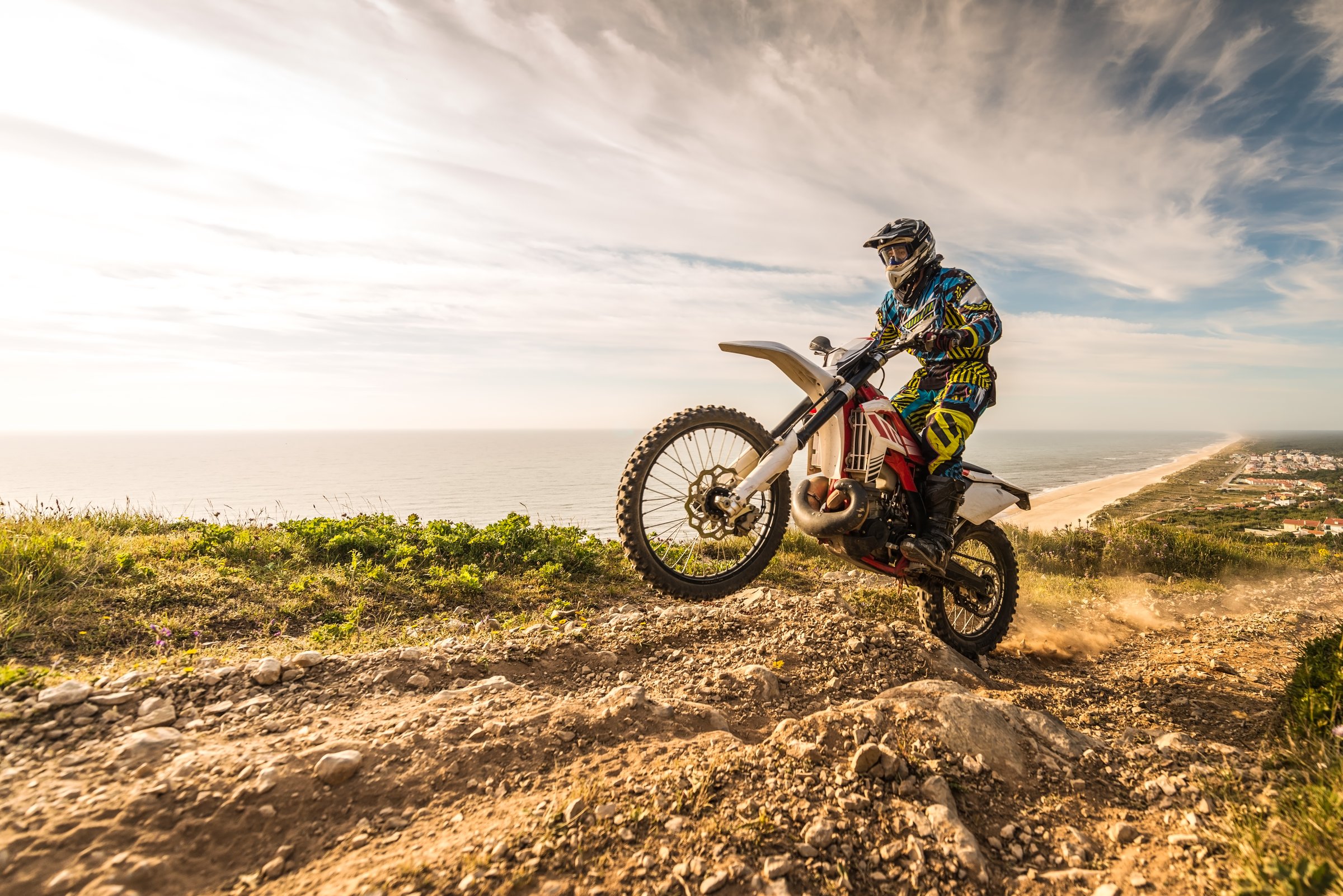 Enduro rider climbing a steep slope against a beautiful sunset on a seascape