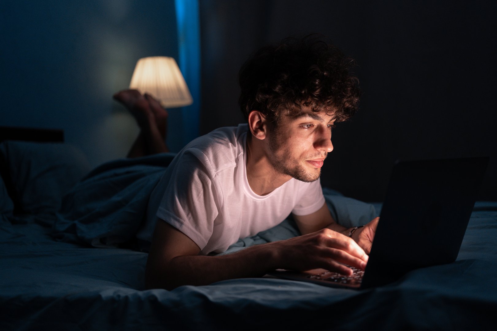 Young internet addict man networking concentrated late at night on bed with laptop in social media addiction or workaholic businessman concept