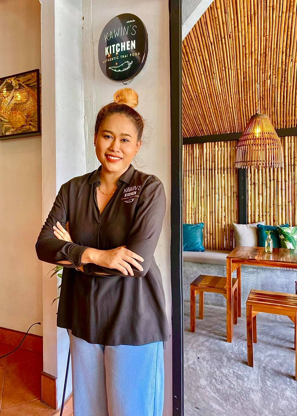Woman in a black shirt standing in a cozy restaurant with bamboo decor and wall art.