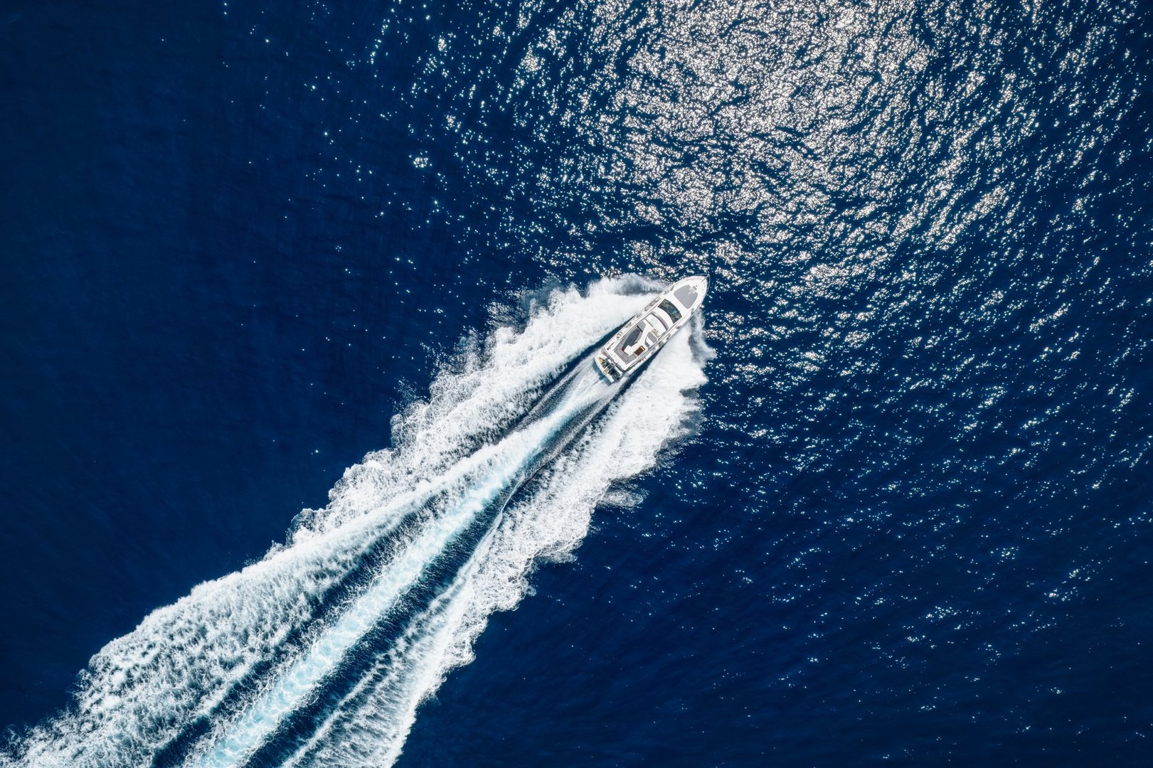 High aerial top view of a luxury yacht cruising with high speed over blue ocean leaving a trail of bubbles and waves behind