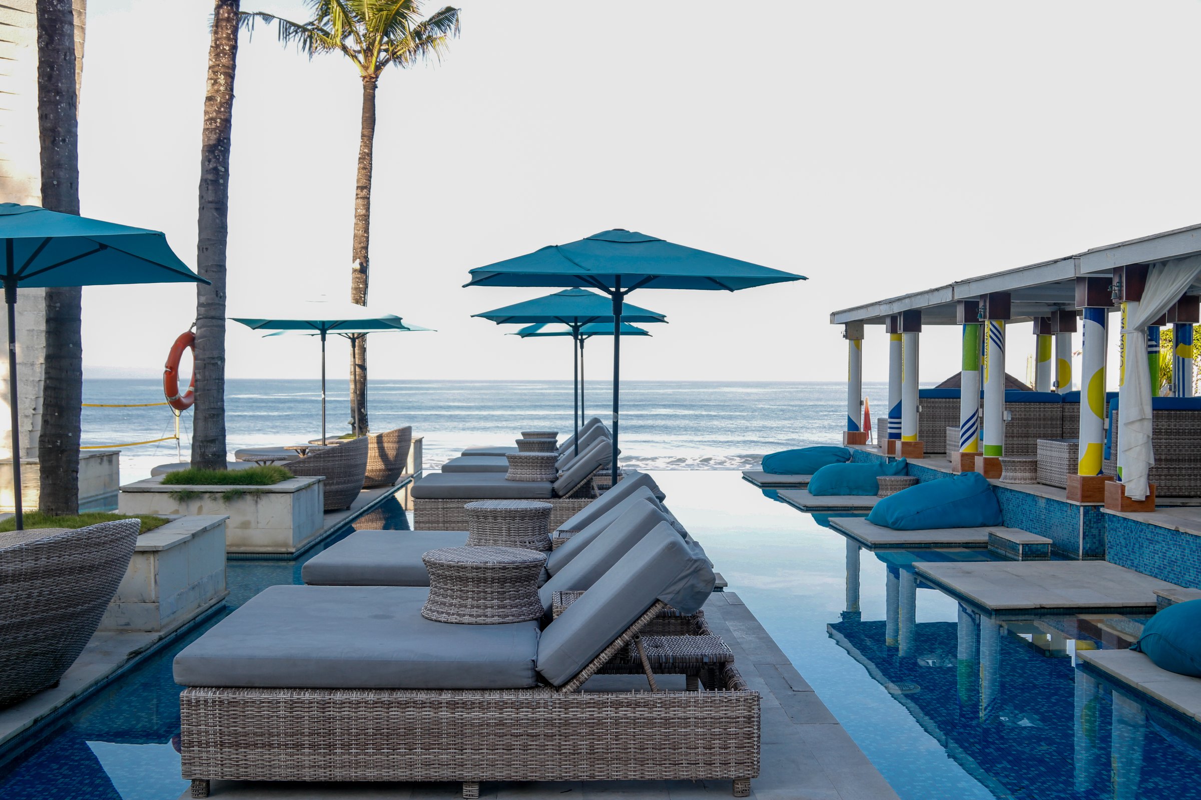 lounge chairs in the pool near the beach under blue beach umbrellas
