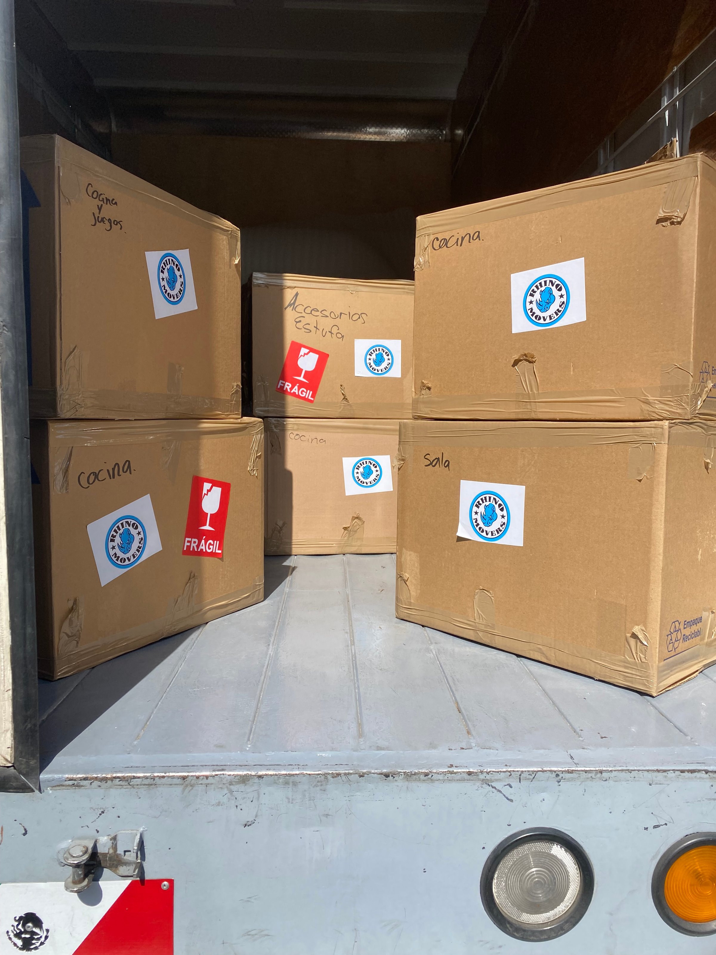 Cardboard boxes labeled "Cocina" and "Sola" in a truck, with fragile stickers and packing symbols visible.