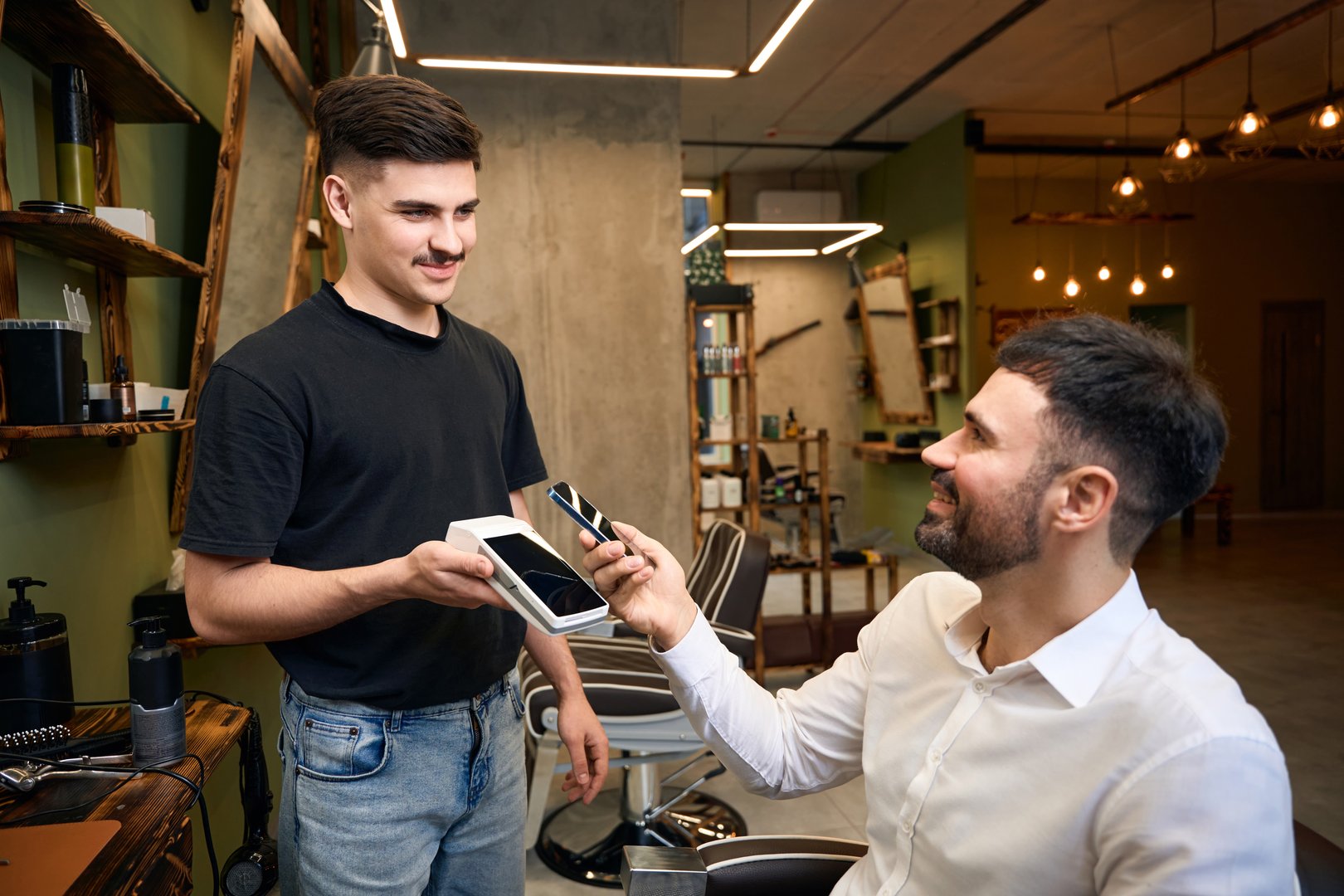 Client paying for hair cutting in barbershop with smartphone and pos terminal