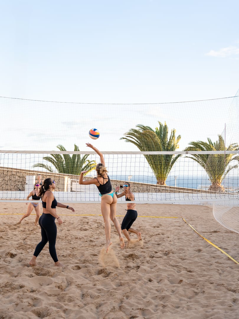 Women athletes jumping and hitting ball during beach volleyball game on sunny beach