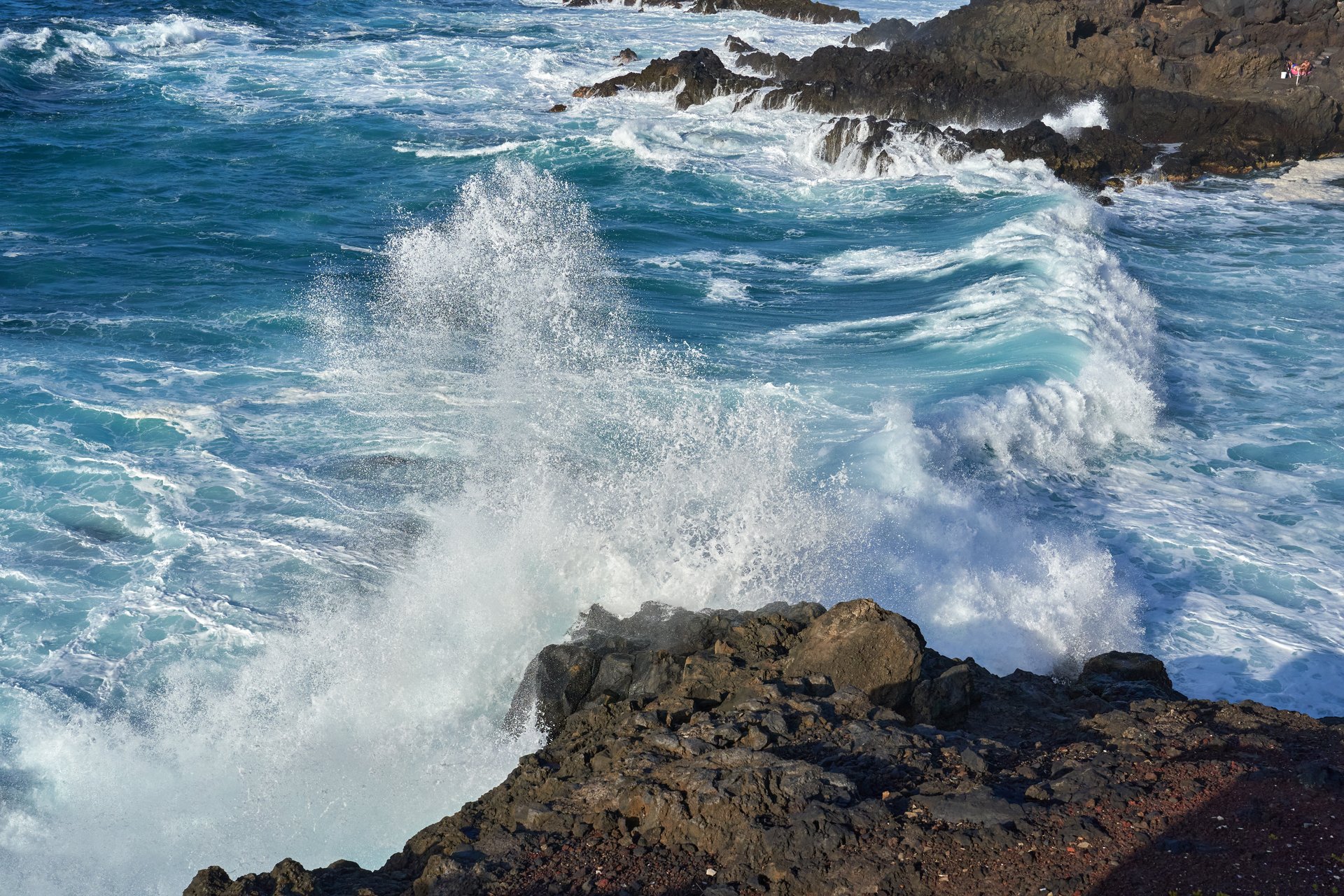 Powerful ocean waves crashing against a rocky coastline, creating white foam and spray in Tenerife