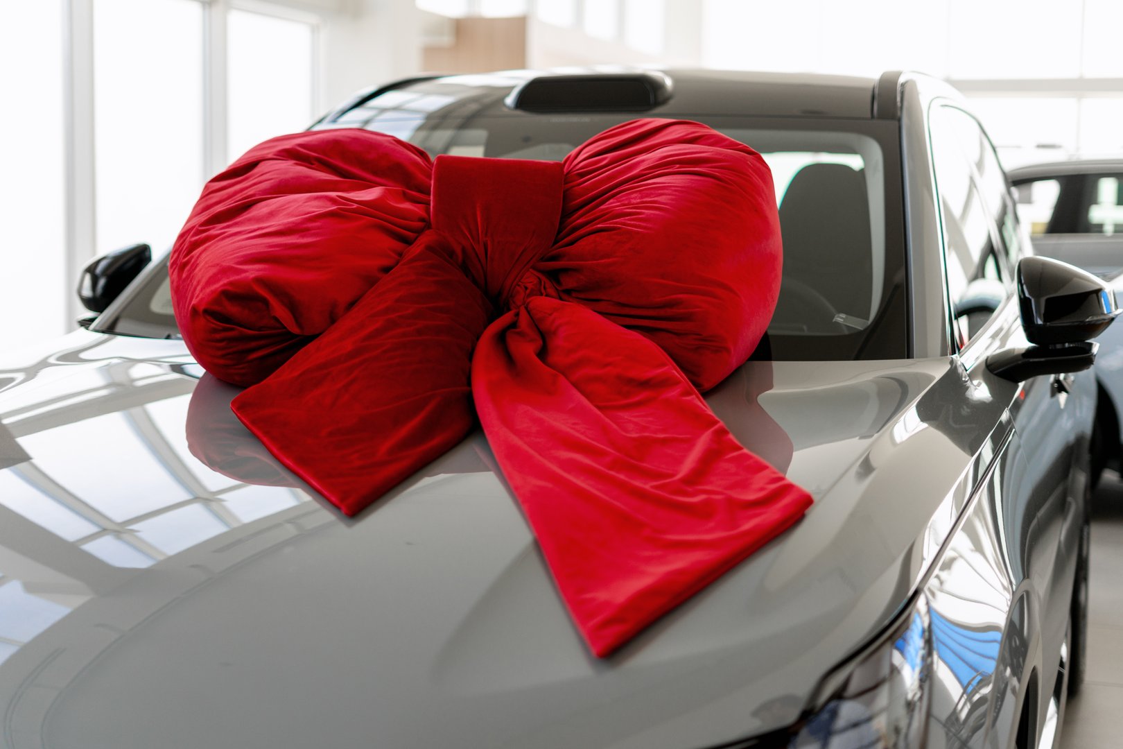 Grey car adorned with a large red bow on the hood, symbolizing the excitement of gifting a luxurious vehicle for a special occasion