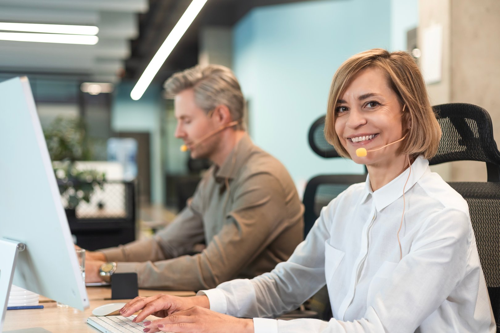 Smiling middle aged female operator call center representative customer support wearing headset working using laptop computer in office