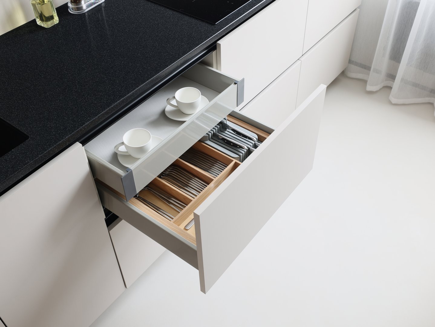 A stylish kitchen drawer displaying a neatly organized arrangement of tableware along with essential utensils