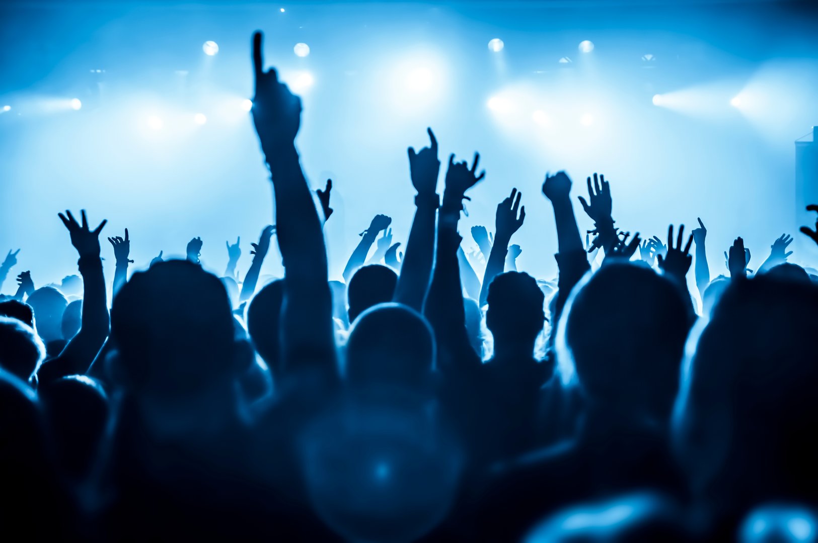 Silhouetted audience with raised hands at a live concert, illuminated by blue stage lights.