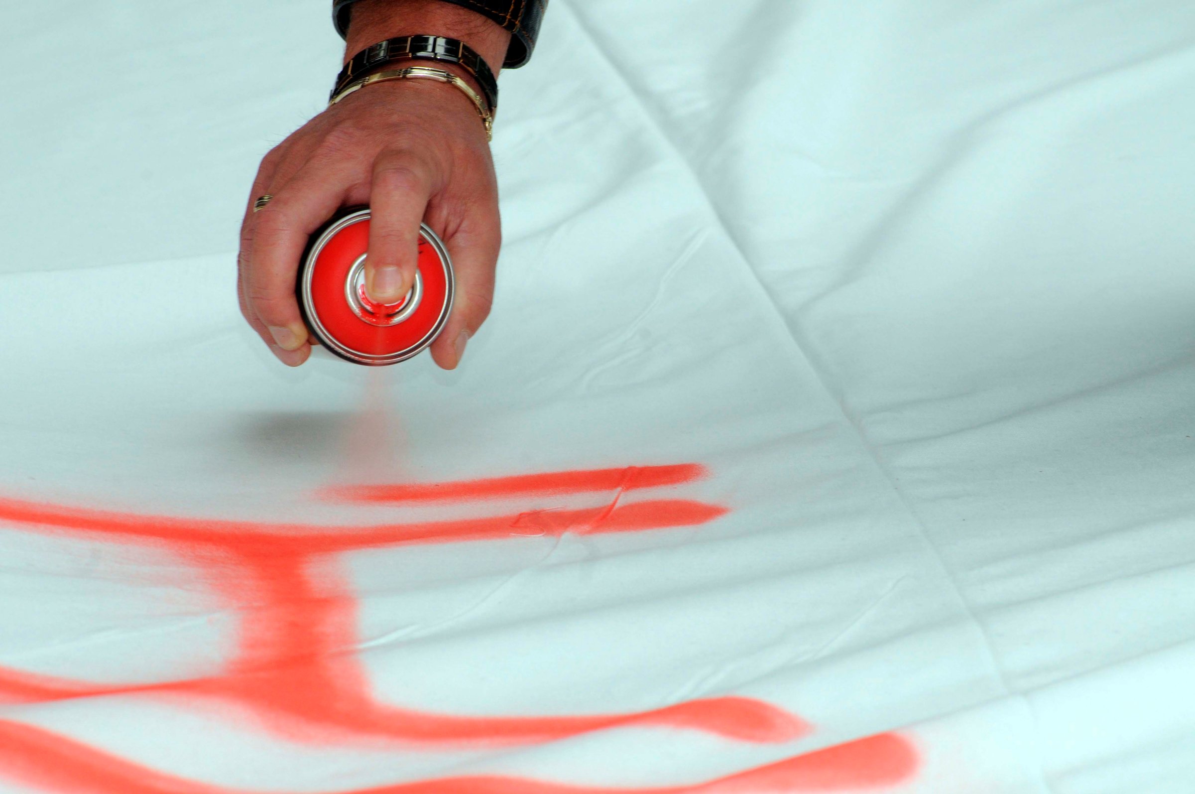 spraying red color with an aerosol can on a white blanket