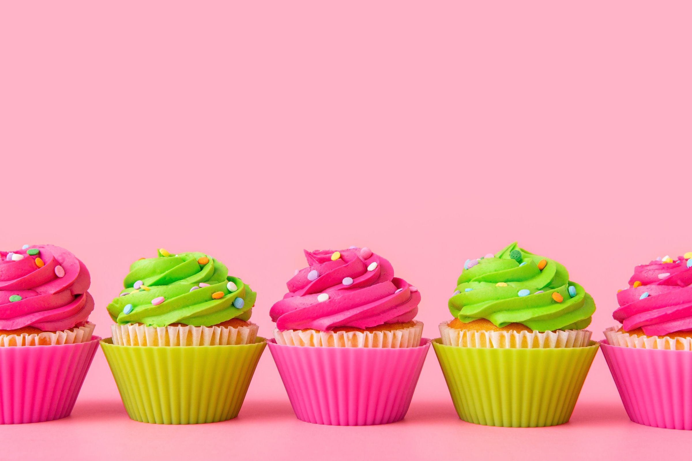Vibrant cupcakes with green and pink frosting and sprinkles on pastel pink background. Bright and cheerful treats perfect for festive celebrations, invitations, or greeting card designs.