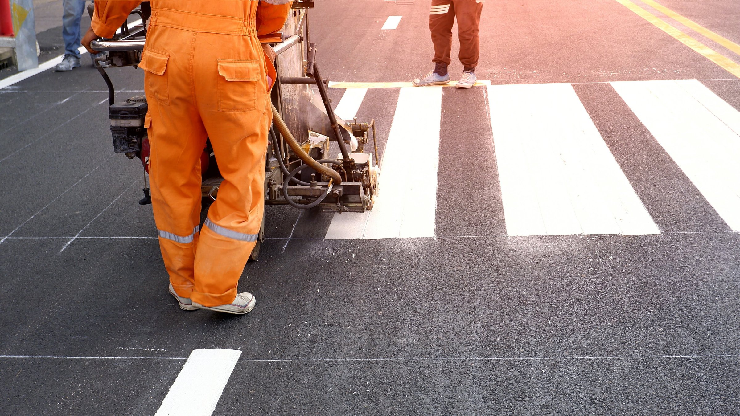 Low section of road workers using thermoplastic spray road marking machine to painting pedestrian crosswalk on asphalt road surface in the city