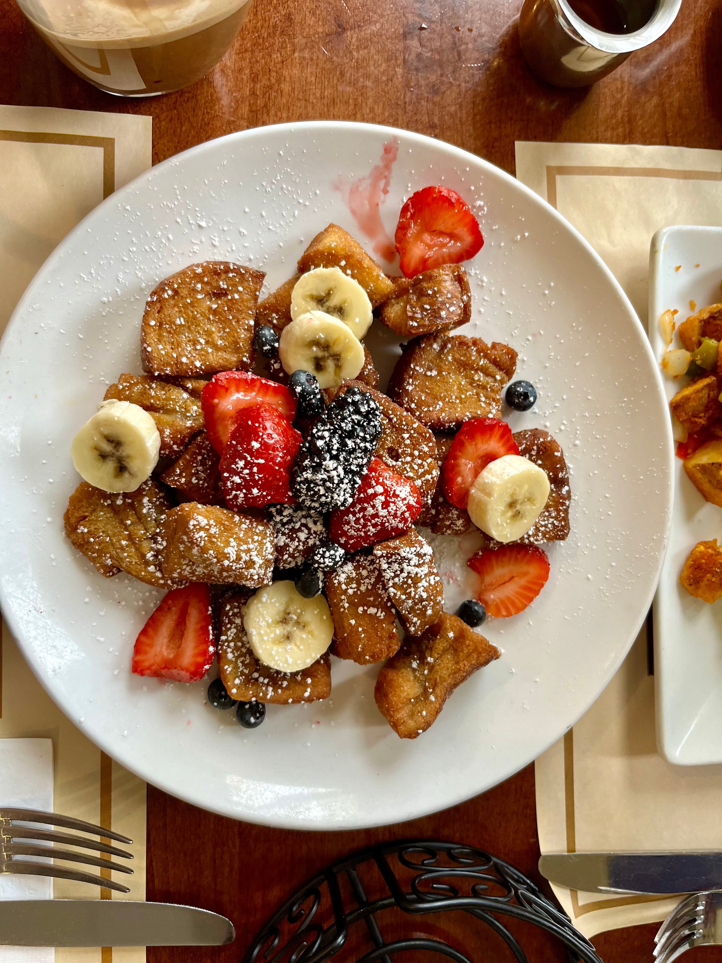 The top down view  of a plate of french toast bites with powdered sugar and fresh fuit.