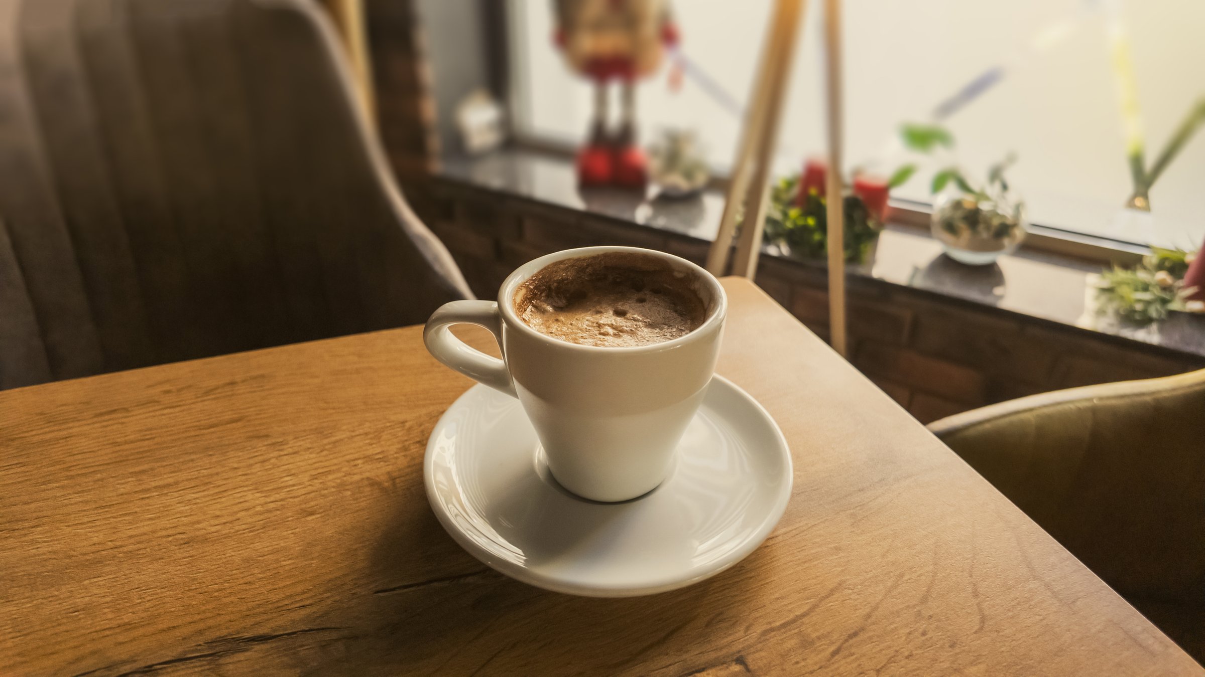 Cup of hot coffee on wooden table in cozy cafÃ©, warm morning light creating peaceful atmosphere and inviting lifestyle scene