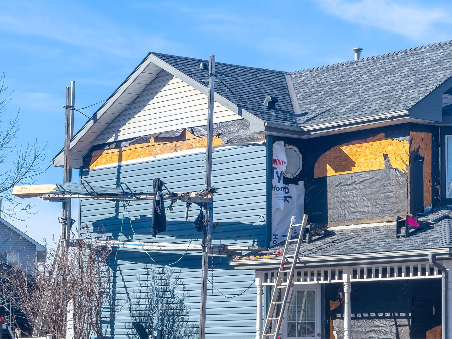 Vancouver, British Columbia, Canada. Mar 10, 2025. A residential house under renovation, with scaffolding, exposed framing, and new light blue siding partially installed. A ladder leans against.