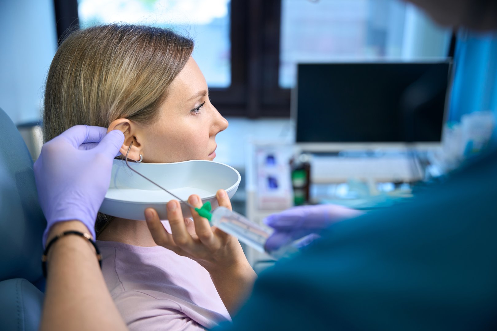 Male otolaryngologist doctor removing earwax with water and a syringe for young woman. Otolaryngology concept