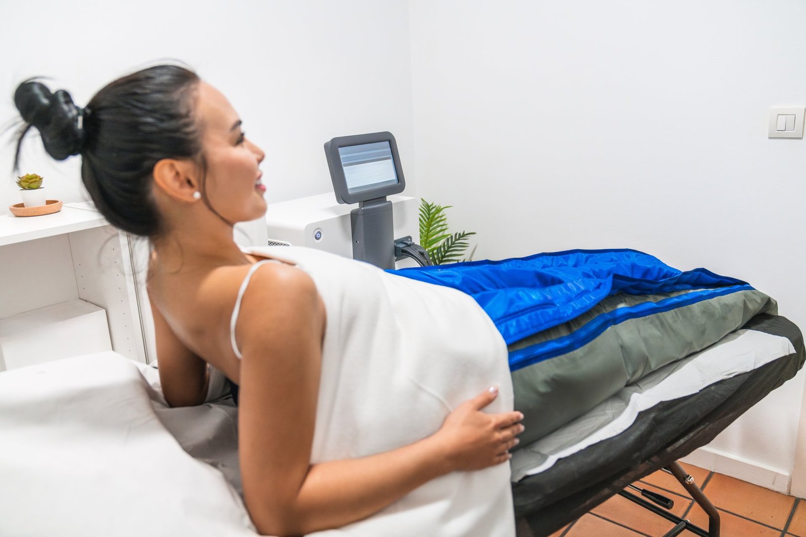 Young woman is lying down on a treatment table, receiving pressotherapy treatment on her legs