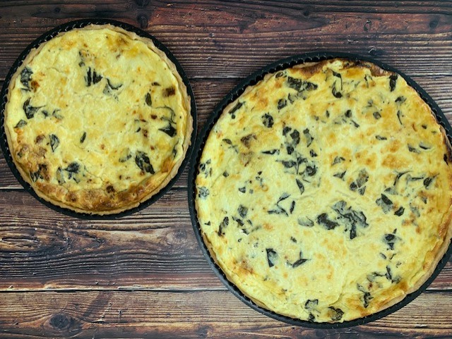 Two mushroom quiches on a wooden table, one larger than the other, both with golden-brown crusts.