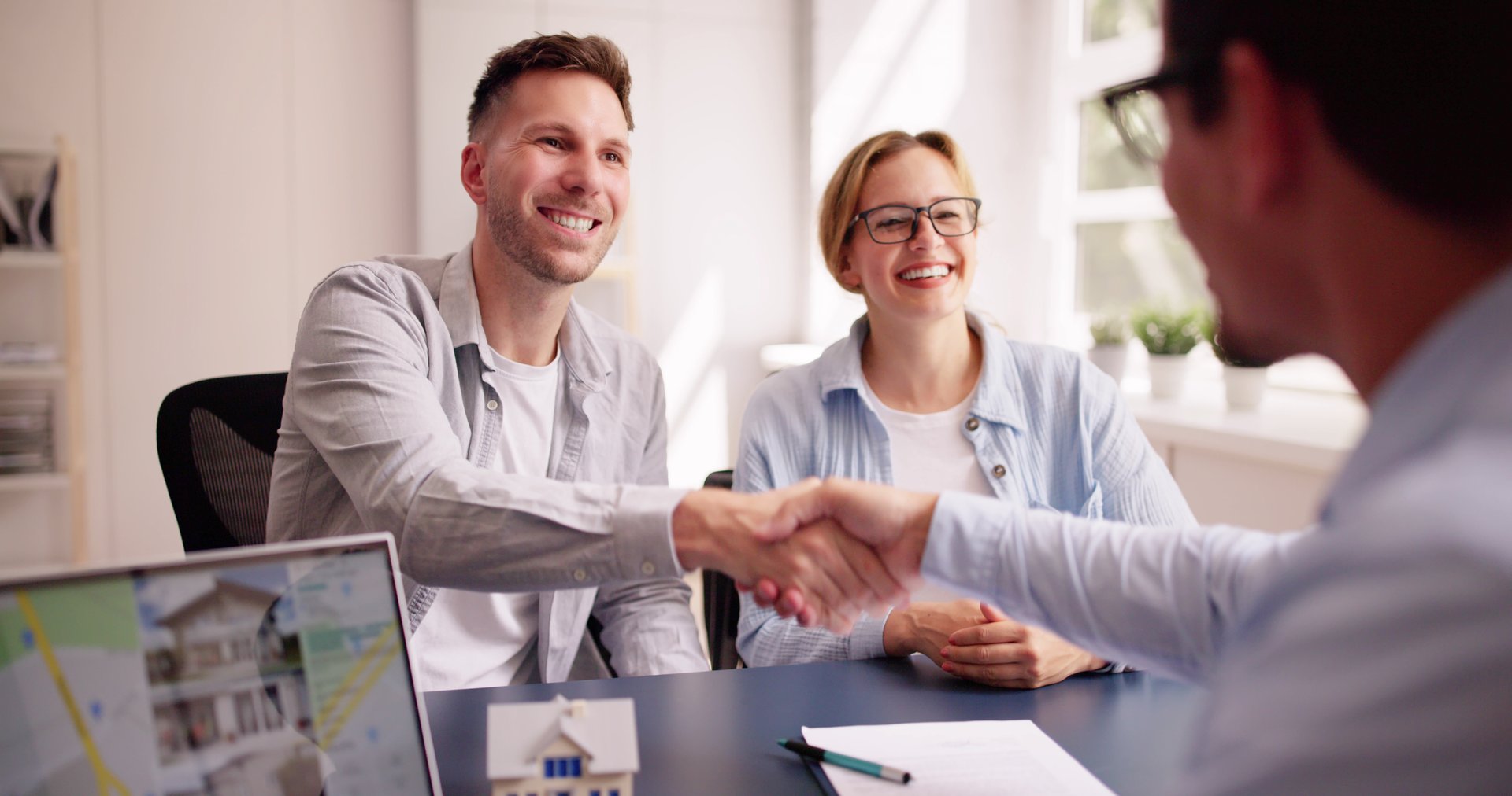 Happy Hispanic Real Estate Agent Shows House to Young Latinx Couple on Laptop at Office Desk for Mortgage Consultation.