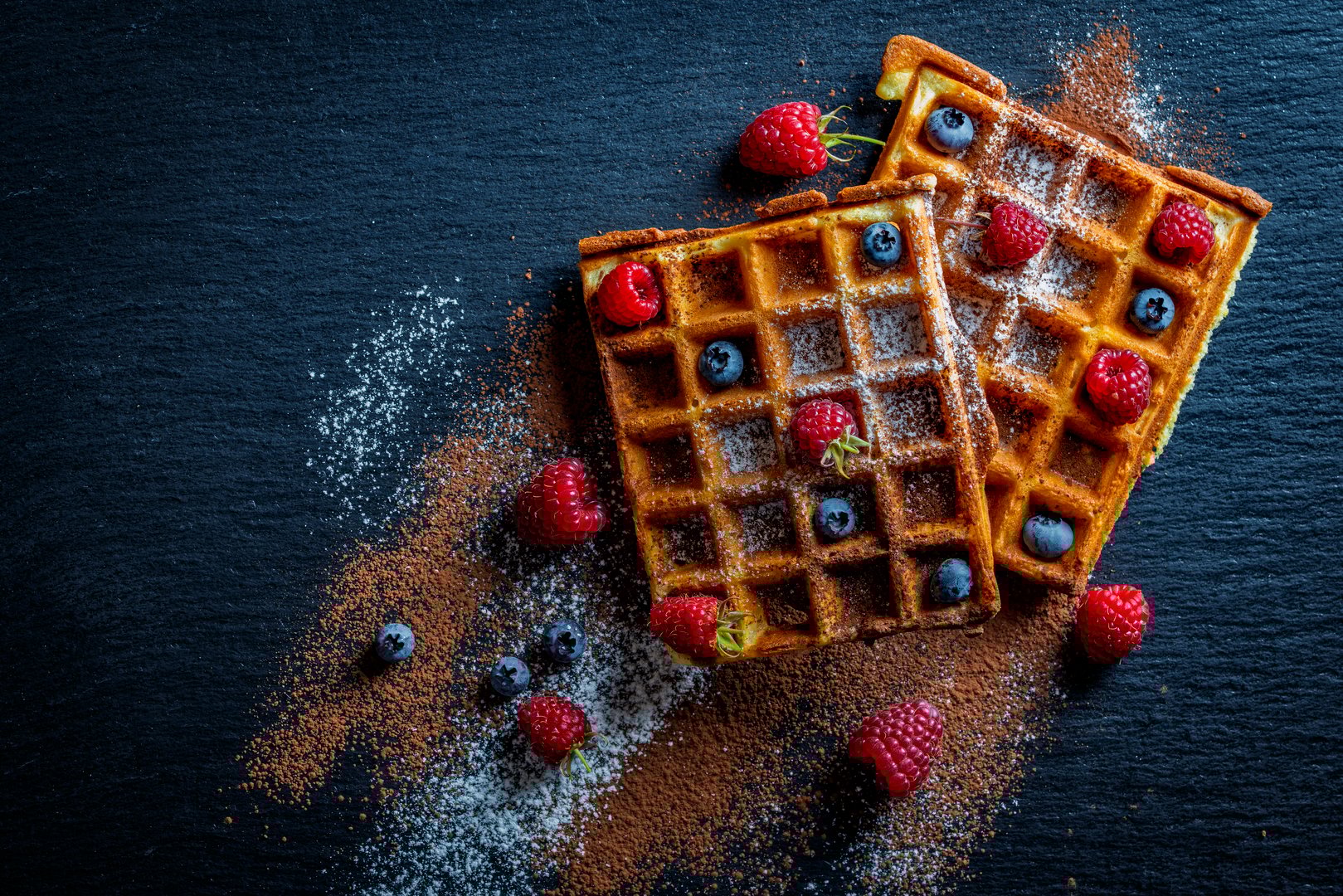 Fresh baked berry Belgian waffle with raspberries and blueberries on black a plate for breakfast, close up, top view. Culinary, cooking, bakery concept. Food recipe background. Sweet waffles