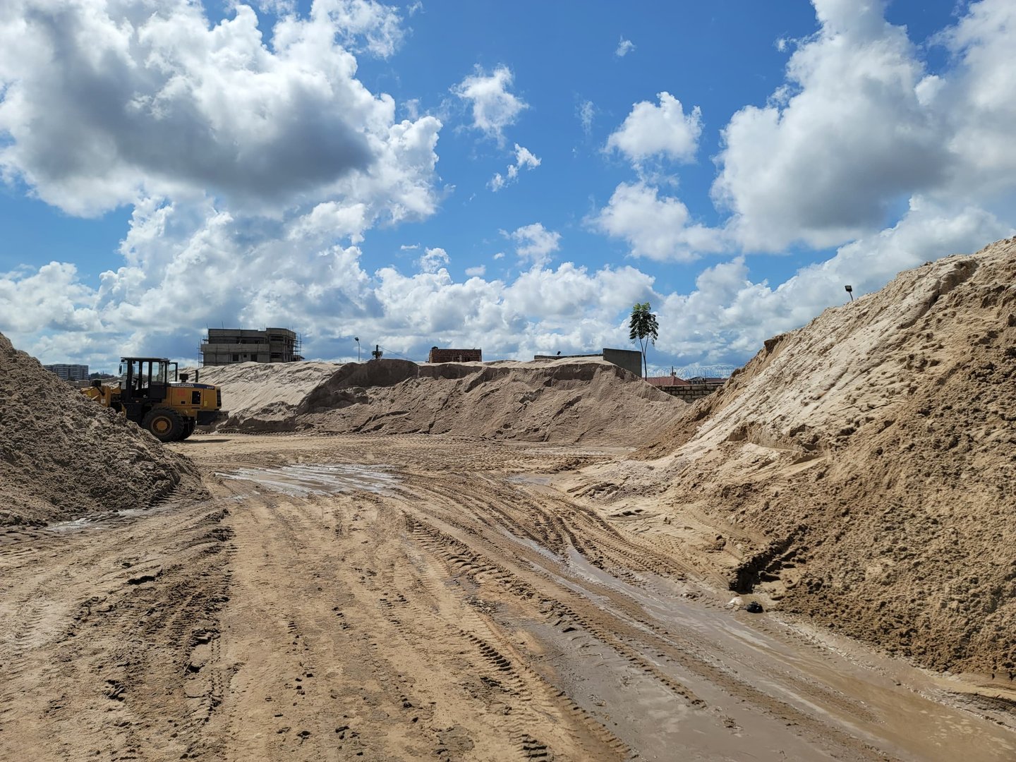 Construction site with piles of sand, a bulldozer, and cloudy sky above.