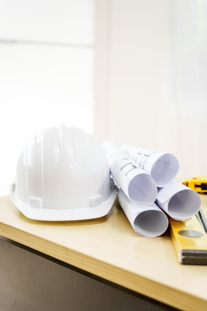 An architect's desk with blueprints and a white hardhat sits empty, ready for the next project.