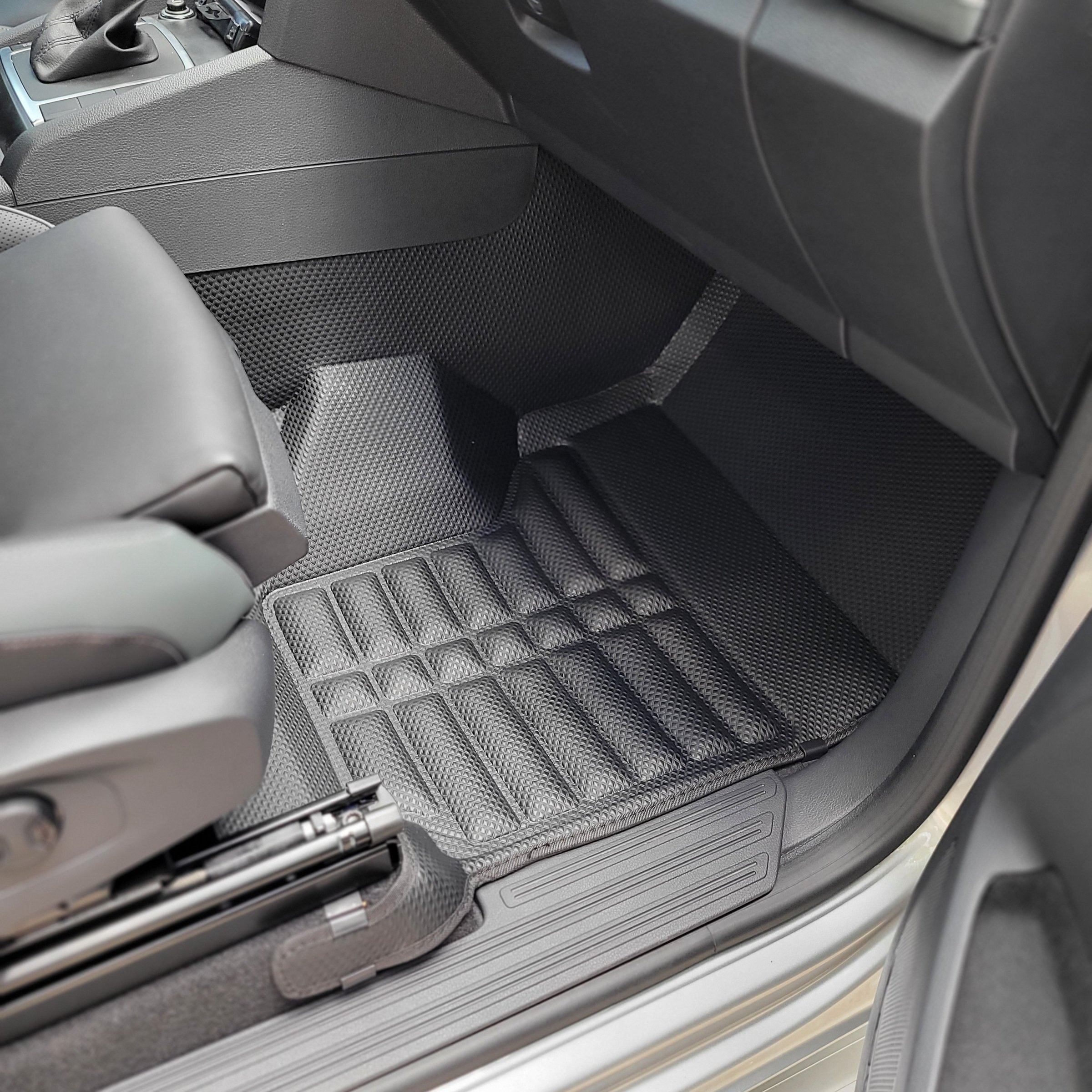 Car interior with textured black rubber floor mat in the front passenger area, showing part of the seat and door sill.