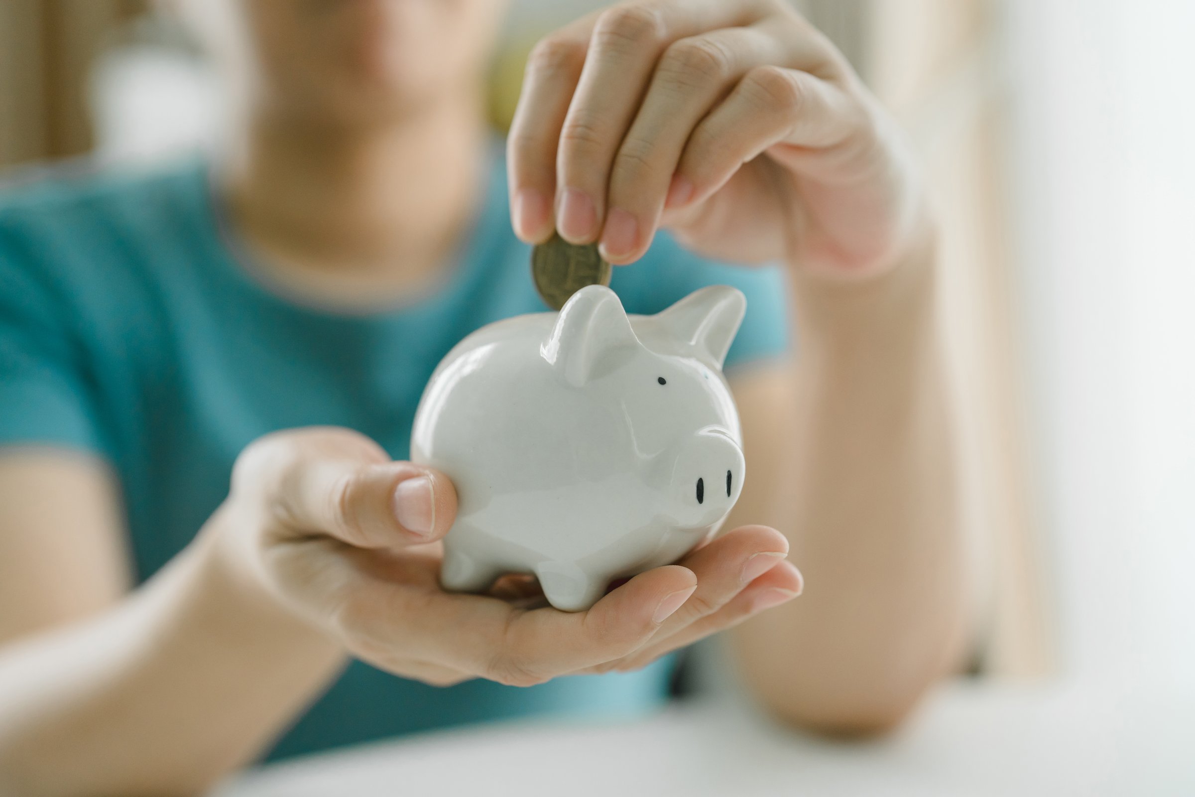 Woman Depositing Coins into White Piggy Bank. Concept of Saving Money and Financial Growth, Featuring Stacks of Coins and a Hand Holding the Piggy Bank.