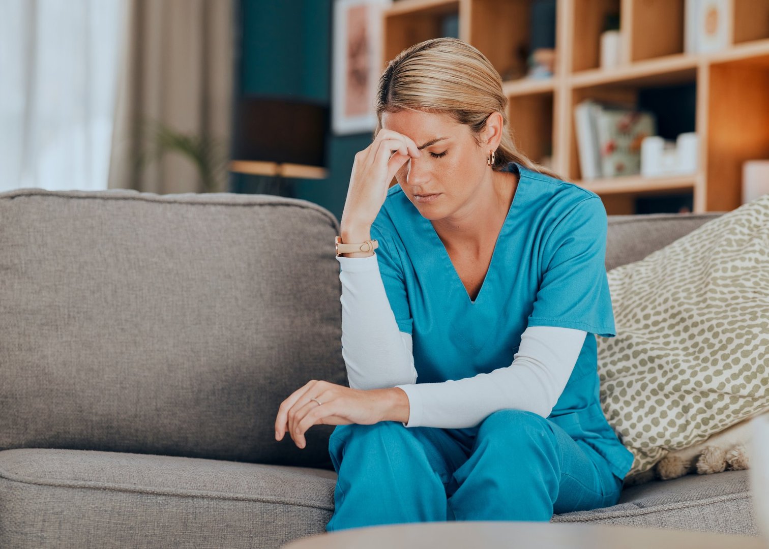 Worry, stress and burnout woman nurse sitting on sofa of modern apartment home, work break and professional rest. Hand on head, anxiety and tired nursing professional distress on couch of living room