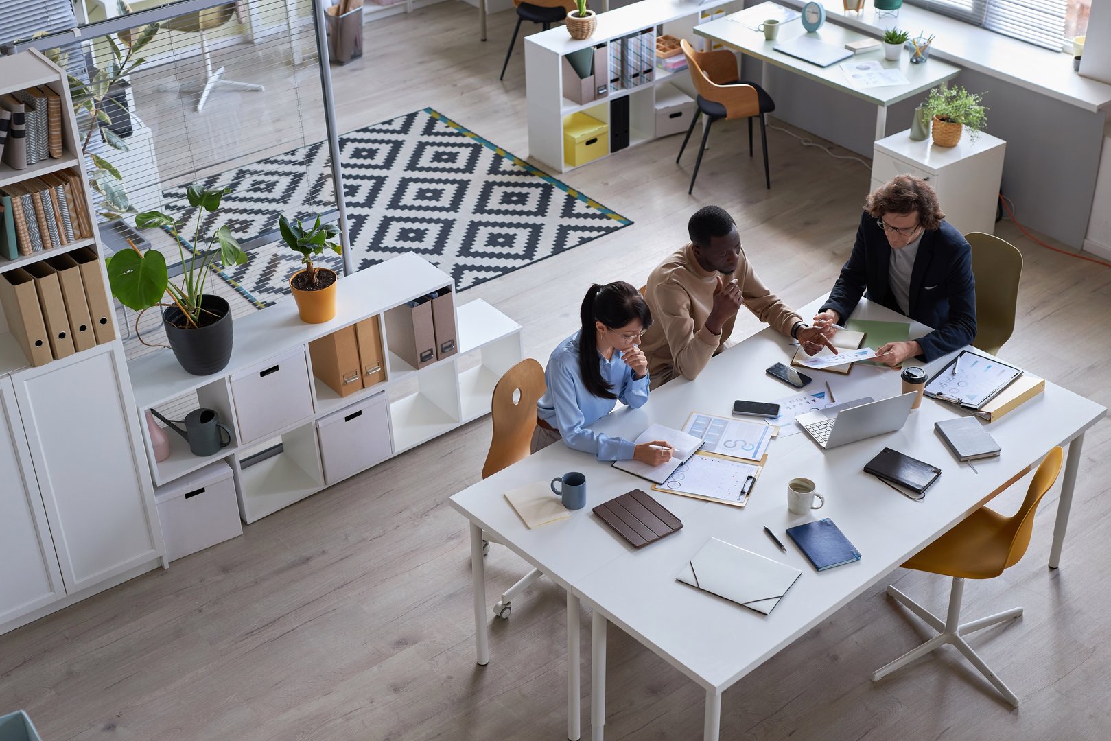 Wide angle top view of business team working together at meeting table in office and pointing at documents with data charts, copy space