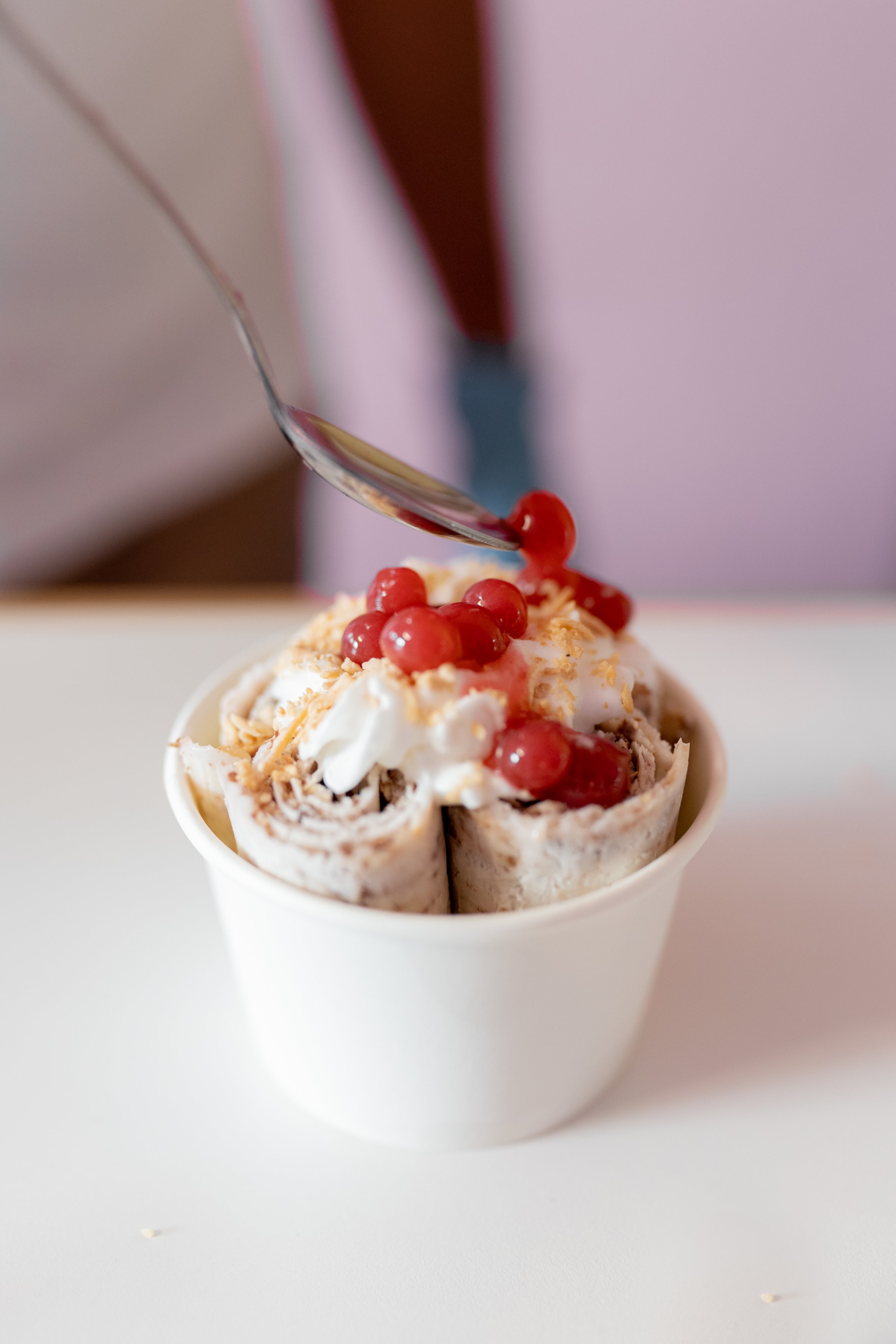 A worker is decorating a rolled ice cream tub with strawberry bubble toppings on top with a spoon. Concept of new small business