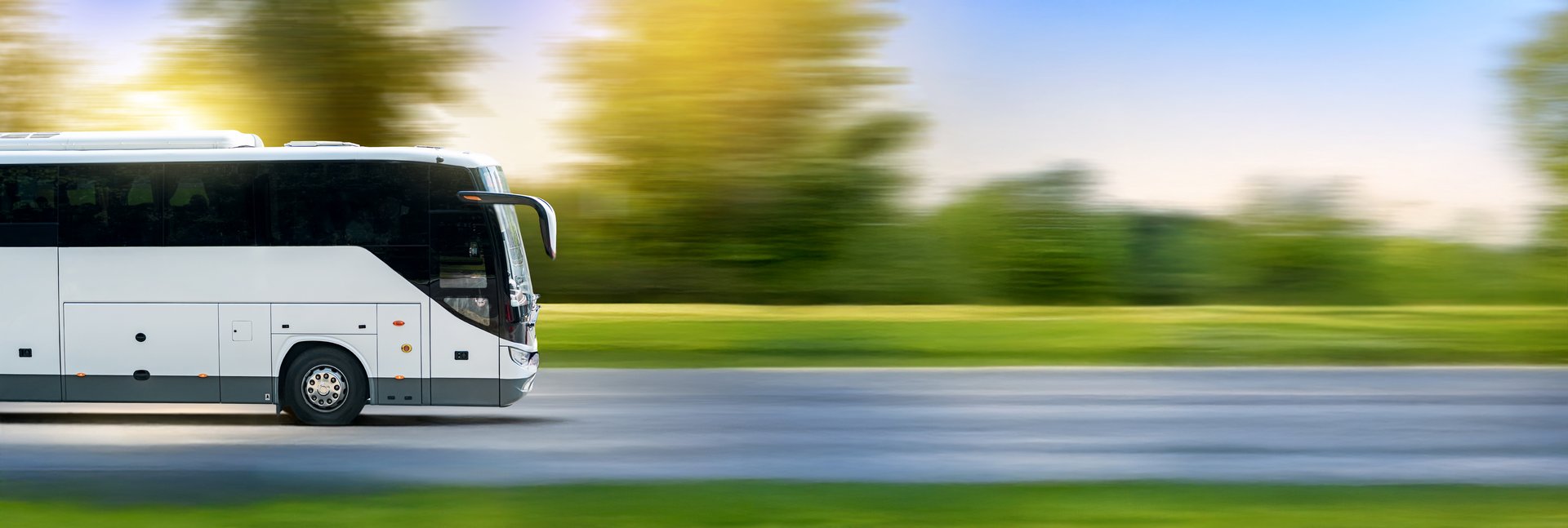 White bus on asphalt road in countryside landscape at sunset