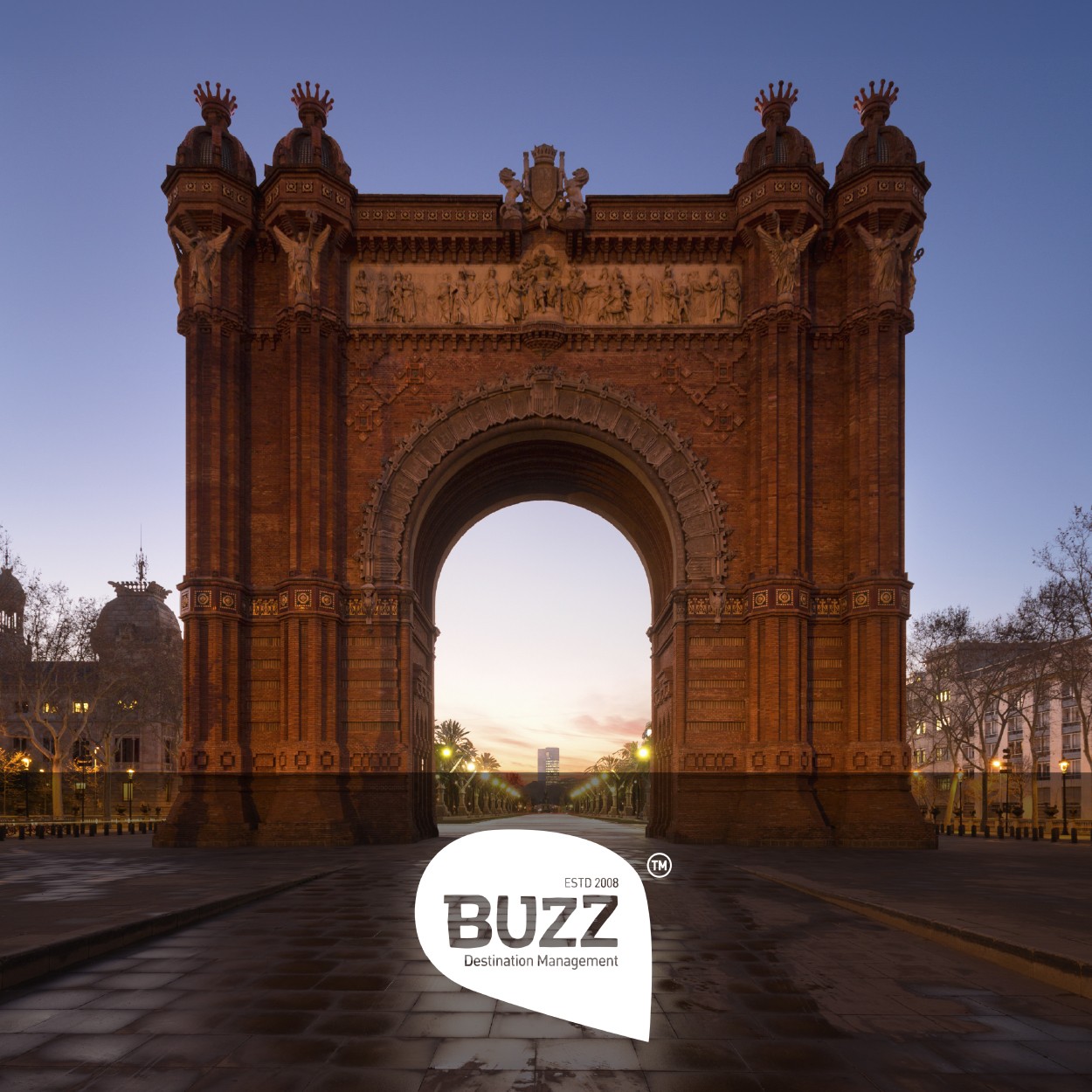 An archway, resembling Barcelonas Arc de Triomf, at dusk with a path leading through. Buzz logo at the bottom center.