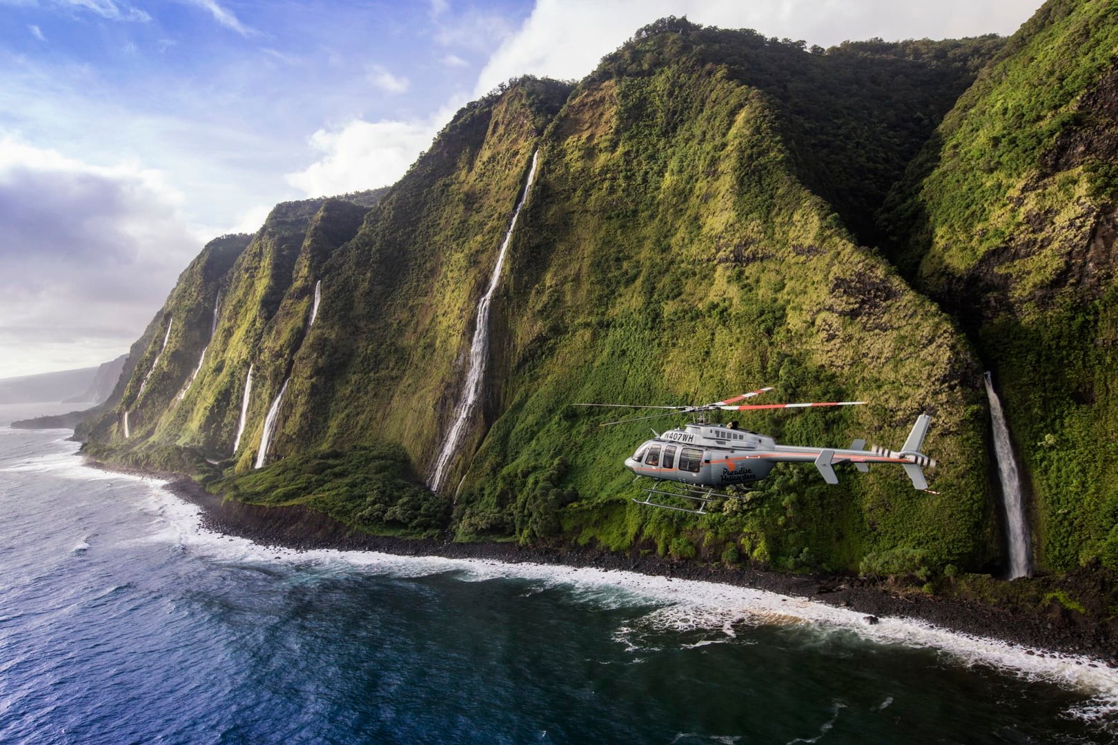 Helicopter tour over Kohala Coast waterfall with stunning aerial view of cascading water and lush tropical landscape