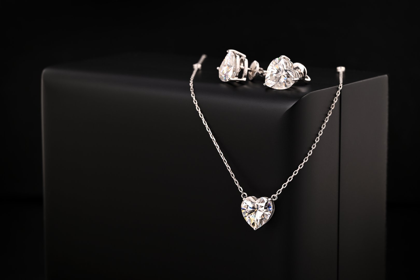 A set of diamond jewelry including a necklace and earrings. The necklace is a heart pendant and the earrings are diamond shaped