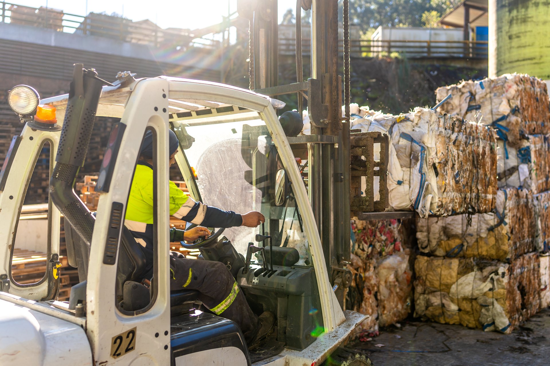 Male worker driving the forklift while loading bales of plastic at the recycling center