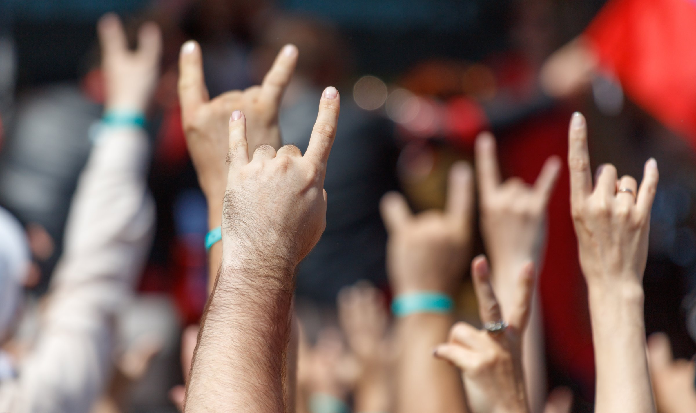 A group of people are holding up their hands with the fingers spread out and the thumbs up. Concept of excitement and enthusiasm, possibly at a concert or a sporting event