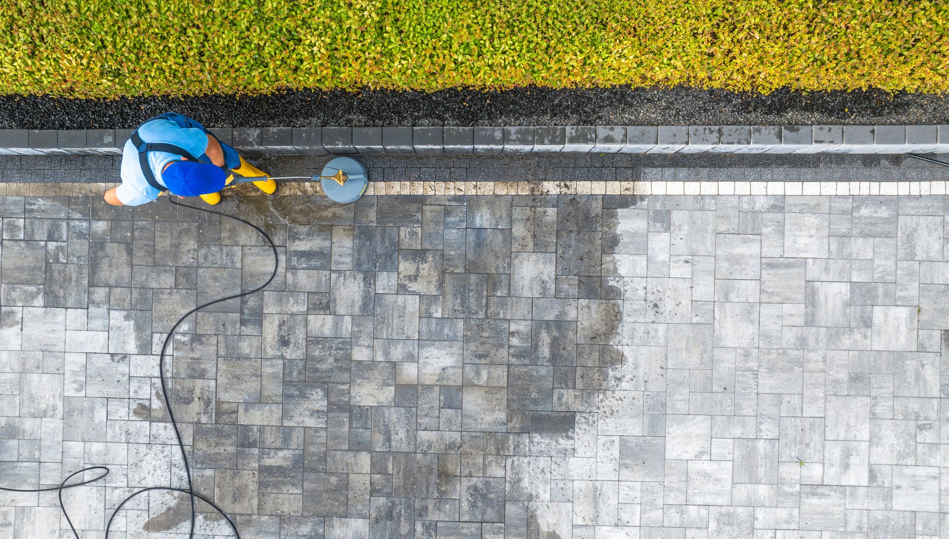 A worker uses a pressure washer to clean a stone patio, revealing a fresh and tidy surface in a well-maintained outdoor area.